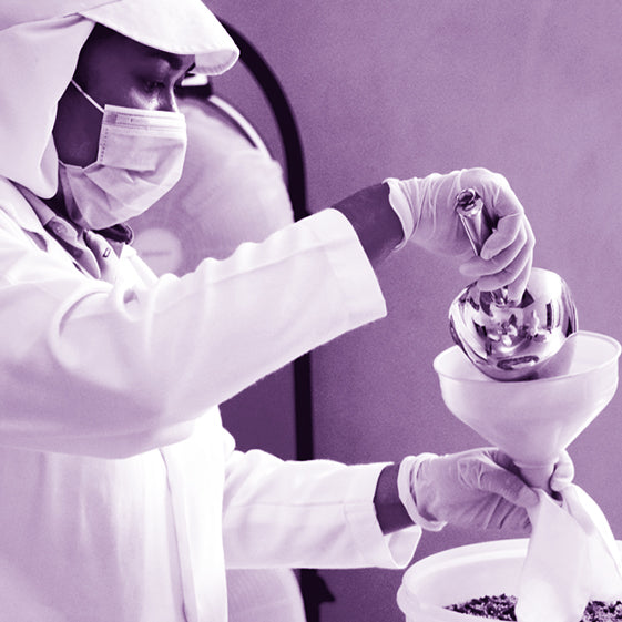 A woman in a lab coat and face masks measures a substance in a chemical lab.