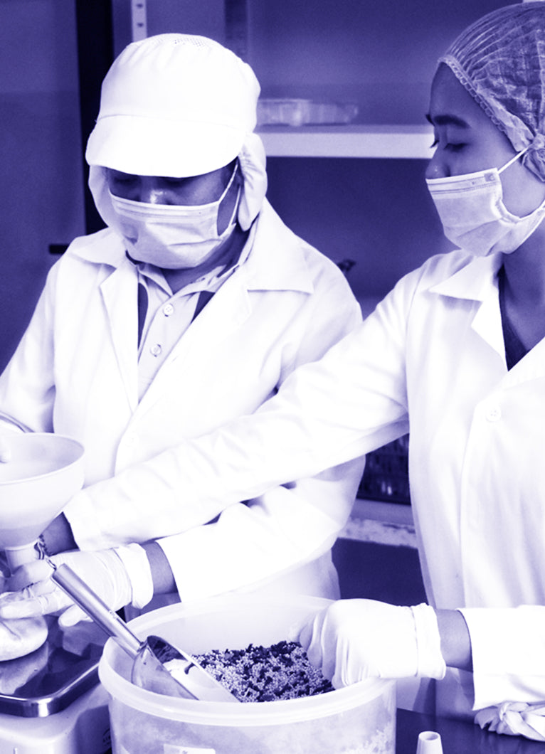 Two women in lab coats and face masks measuring a substance in a chemical lab.