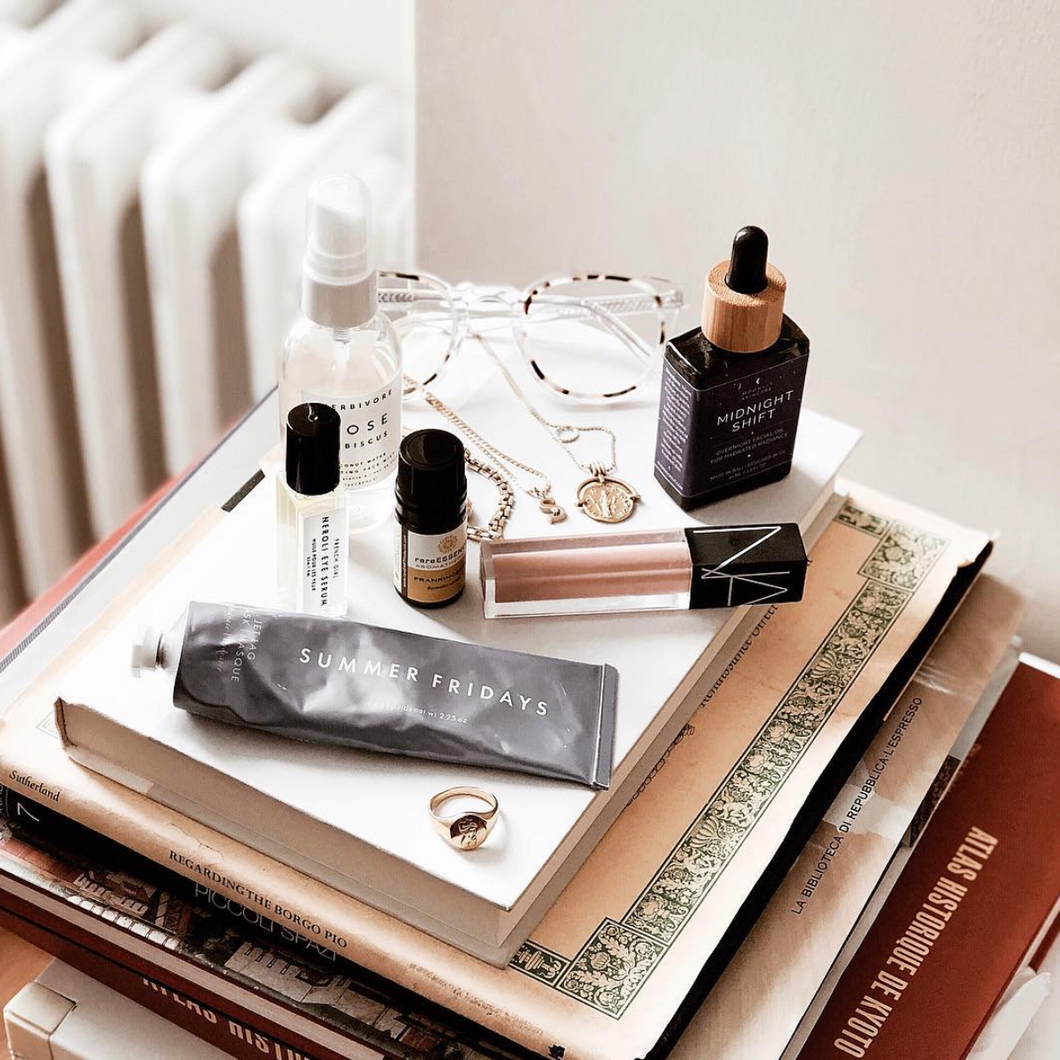 A bottle of Midnight Shift Overnight Facial Oil on top of a stack of book with other beauty products