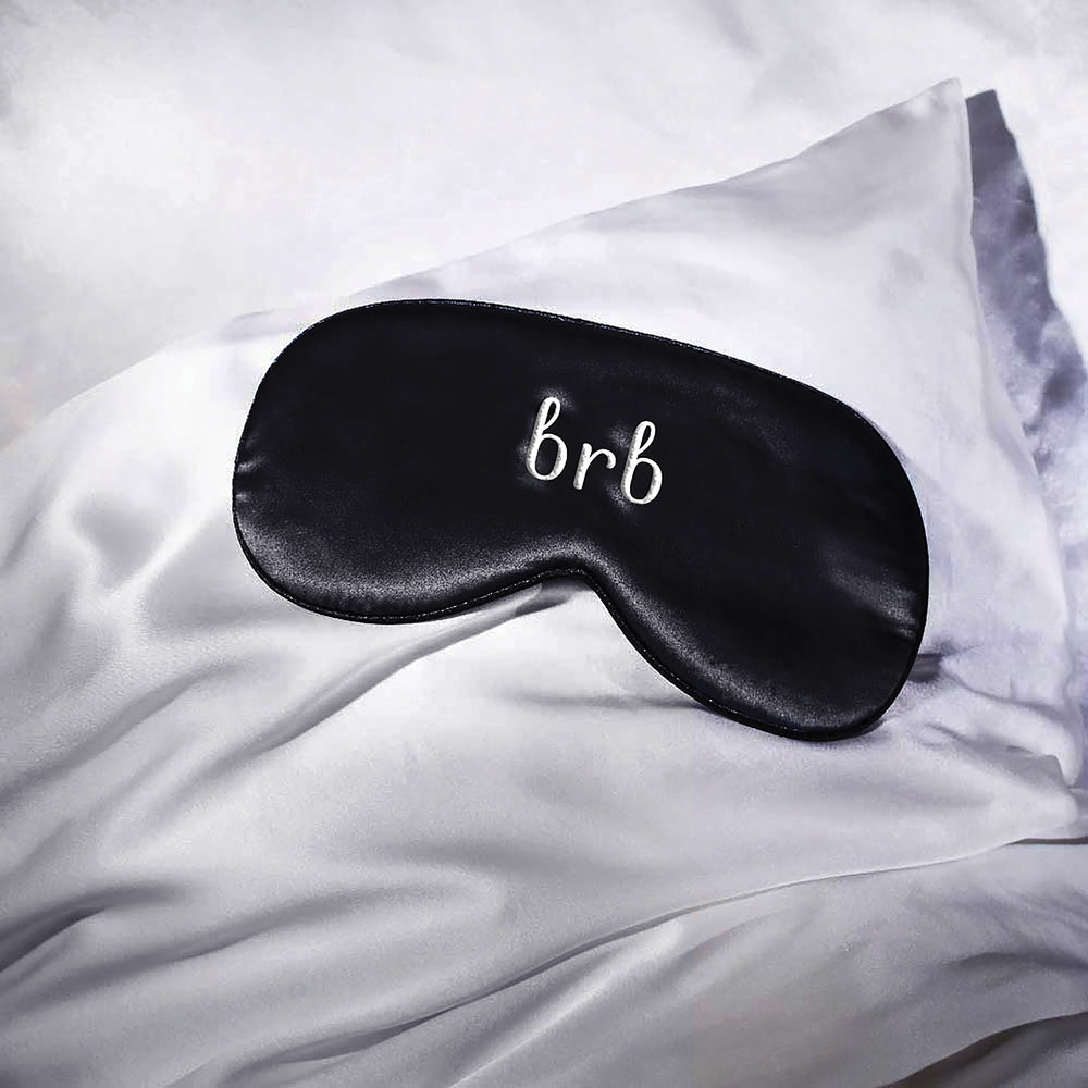 Moonlit Skincare's brb silk eye mask lying on Moonlit Skincare's silk pillowcase in white.