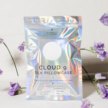 'Cloud 9' Ivory White Silk pillowcase in iridescent packaging standing upright against floral backdrop