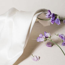'Cloud 9' Ivory White Silk pillowcase lying against purple flowers 