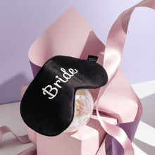 Bride silk eyemask on crystal ball with pink paper and ribbon surrounding it on purple background