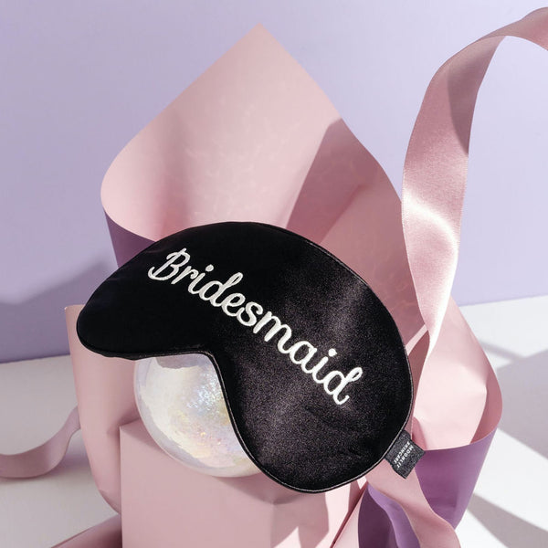 Bridesmaid silk eyemask on crystal ball with pink paper and ribbon surrounding it on purple background