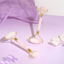 Two Moonlit Skincare Rose Quartz Facial Roller Tool with purple paper, ribbon, and white flower petals surrounding it on purple background