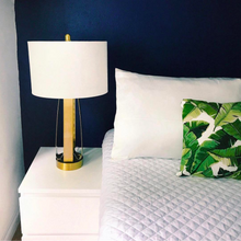 White Bedside with white and gold lamp, pillow fitted with Cloud 9 Silk Pillowcase in Ivory White, and leaf-patterned cushion.